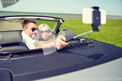 Image of happy couple in car taking selfie with smartphone