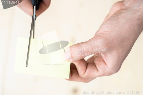 Image of A man is cutting a sheet of yellow paper using metallic scissors