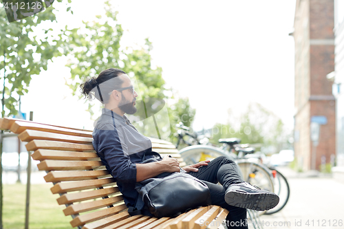 Image of man with backpack sitting on city street bench