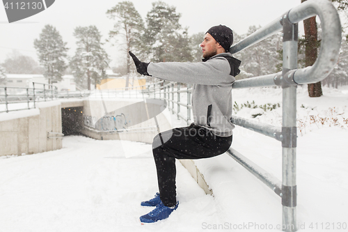 Image of sports man doing squats at fence in winter