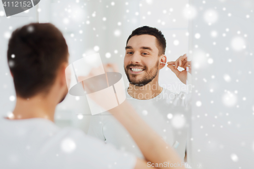 Image of man cleaning ear with cotton swab at bathroom