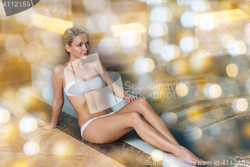 Image of happy woman in bikini sitting at swimming pool