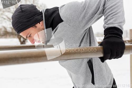 Image of young man exercising on parallel bars in winter