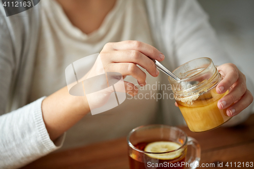 Image of close up of woman adding honey to tea with lemon