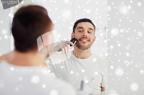 Image of man shaving beard with trimmer at bathroom