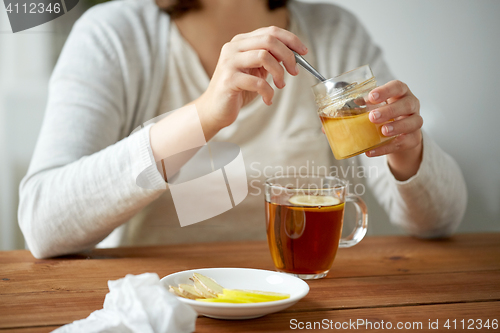 Image of close up of woman adding honey to tea with lemon