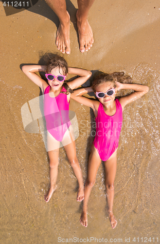 Image of Two girls lie on his back on the surf of the sea sandy beach, there are a number of adult human foot