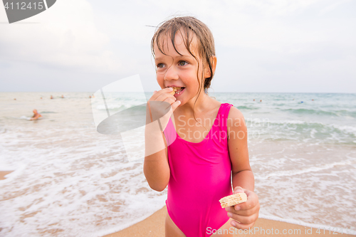 Image of The girl in the pink bathing suit standing on the beach and eating waffle