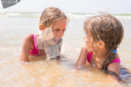 Image of Two girls lying in the shallow water and have fun looking at each other