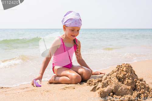 Image of Girl happily looks at the sand pit dug up, sitting on the beach