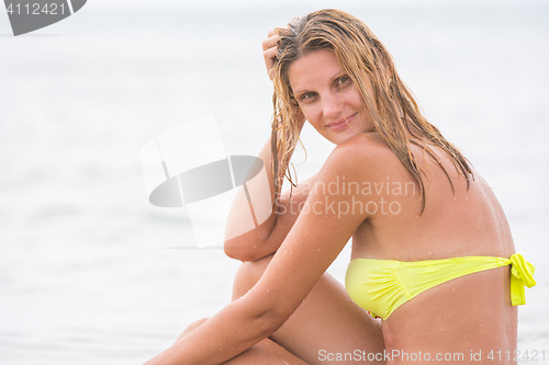 Image of Happy young beautiful girl sitting in a bathing suit against the sea