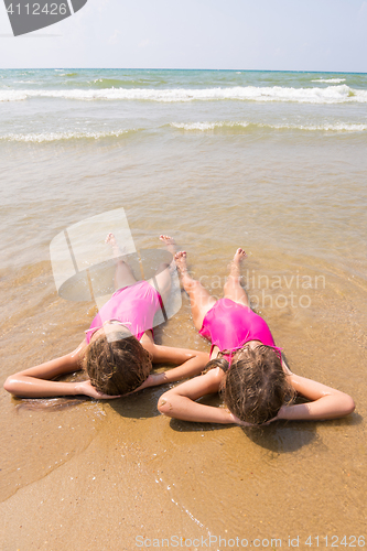 Image of Two girls lie on your back on the sandy beach halfway in the wate