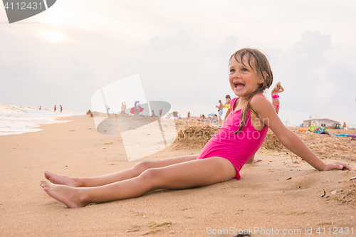 Image of Five-year girl sits on the beach in the evening sea coast on a cloudy day