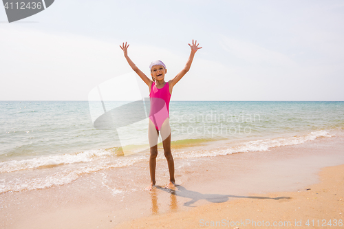 Image of Happy girl lifted her arms up on the sandy shore of the sea