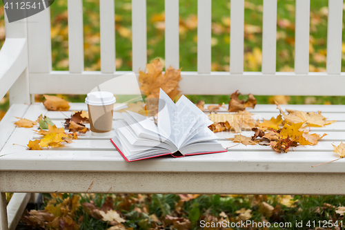 Image of open book and coffee cup on bench in autumn park