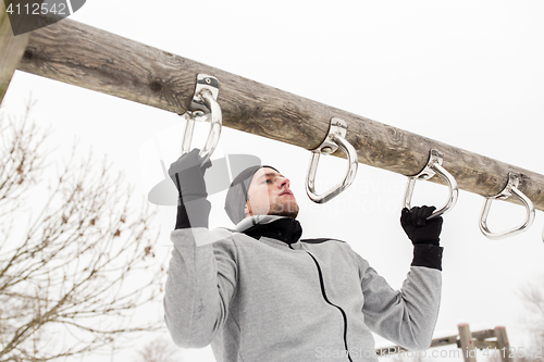 Image of young man exercising on horizontal bar in winter