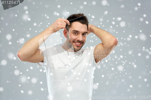 Image of happy man brushing hair with comb over snow