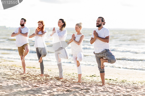 Image of people making yoga in tree pose on summer beach