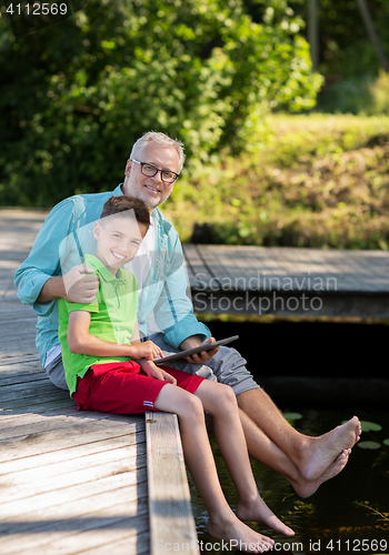 Image of grandfather and boy with tablet pc on river berth