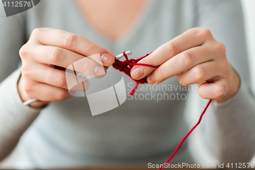 Image of woman knitting with crochet hook and red yarn