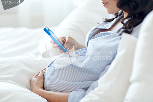 Image of close up of pregnant woman with smartphone in bed