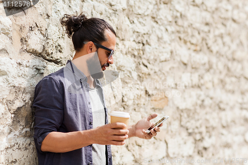 Image of man with smartphone drinking coffee on city street