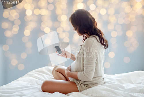 Image of pregnant woman with smartphone in bed