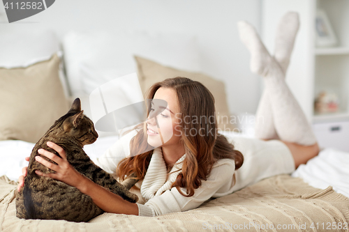 Image of happy young woman with cat lying in bed at home