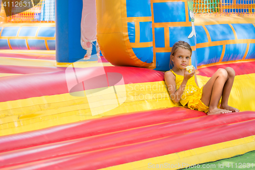 Image of Girl sits at the entrance to an inflatable trampoline and eats an apple