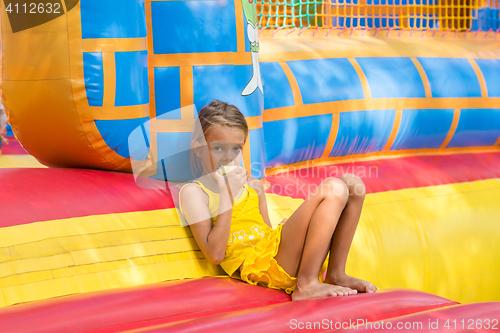 Image of Girl eats an apple sitting on the edge of the inflatable trampoline in amusement park