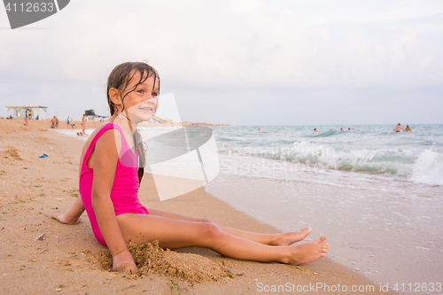 Image of Five-year girl sits on a beach and seaside fun looking into the distance