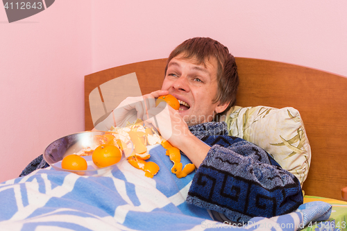 Image of Happy young man biting tangerine lying in bed