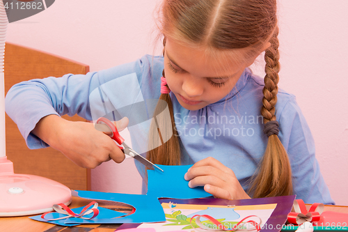 Image of The child cuts off a piece of the blue colored cardboard