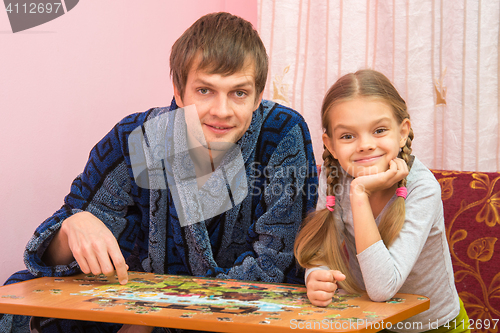 Image of Dad and daughter in the frame looked sitting at the table and collecting puzzles