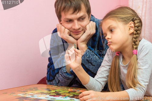Image of Dad with a kind smile looking at her daughter who is considering an element of the puzzle thinking where to put it