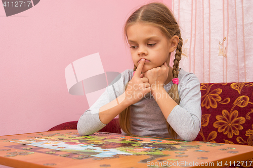 Image of The child is thinking how to assemble a picture from puzzles