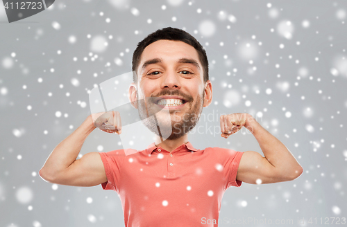 Image of smiling man showing biceps over snow background