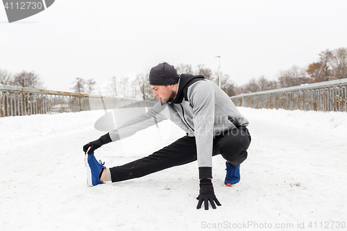 Image of man exercising and stretching leg on winter bridge