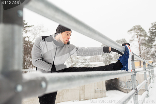 Image of sports man stretching leg at fence in winter