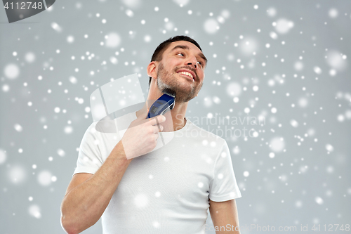 Image of smiling man shaving beard with trimmer over snow