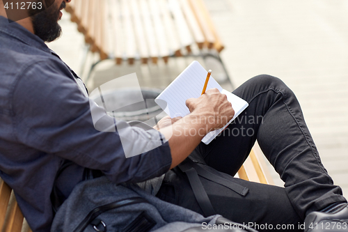 Image of close up of man writing to notebook on city street