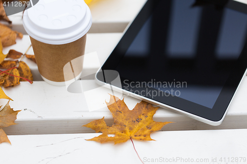 Image of tablet pc and coffee cup on bench in autumn park