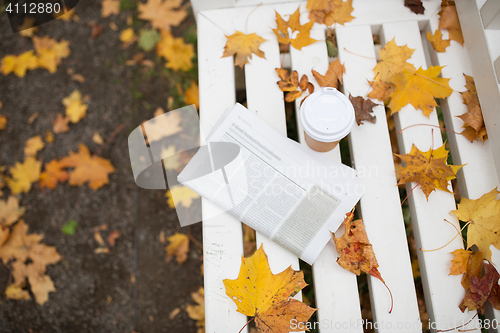 Image of newspaper and coffee cup on bench in autumn park