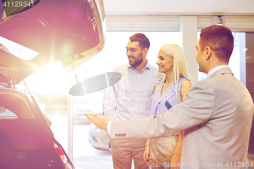 Image of happy couple with car dealer in auto show or salon