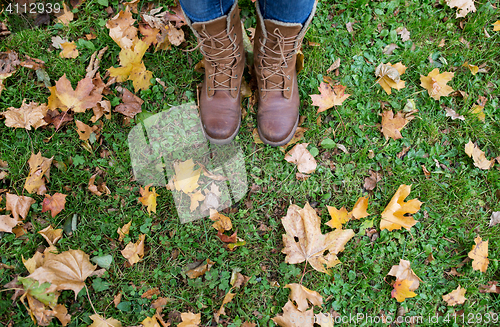 Image of female feet in boots and autumn leaves on grass