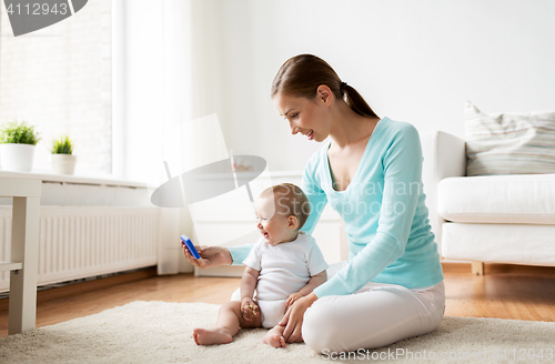 Image of happy mother showing smartphone to baby at home