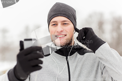 Image of happy man with earphones and smartphone in winter