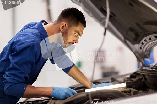 Image of mechanic man with lamp repairing car at workshop