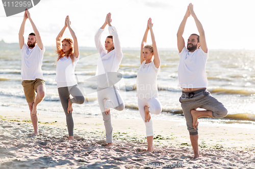 Image of people making yoga in tree pose on summer beach
