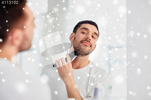 Image of man shaving beard with trimmer at bathroom